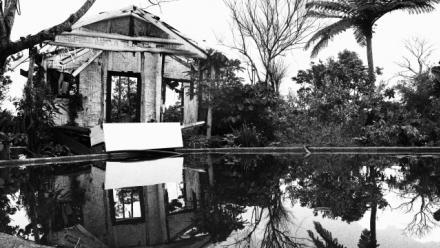 an black and white image of a bamboo hut with reflection over water in a pool. 
